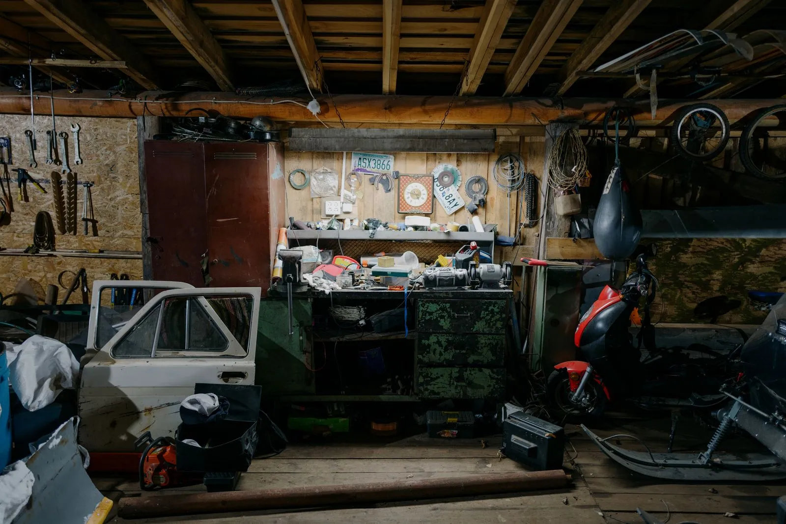 A cluttered home garage: hand tools on the wall, a moped, a workbench and years of accumulated stuff