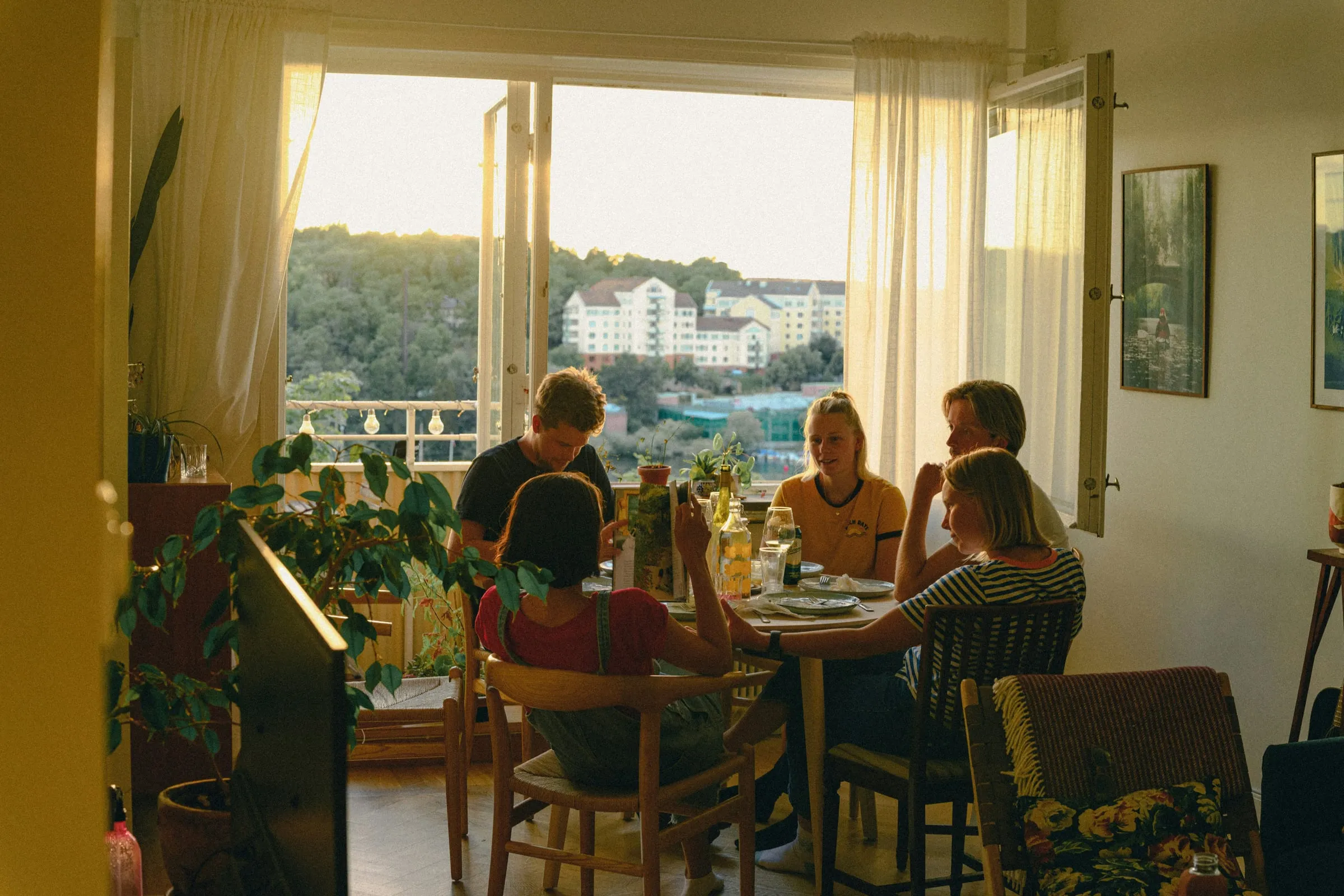 Five friends around a table in a lived-in apartment at golden hour, sunset through the window