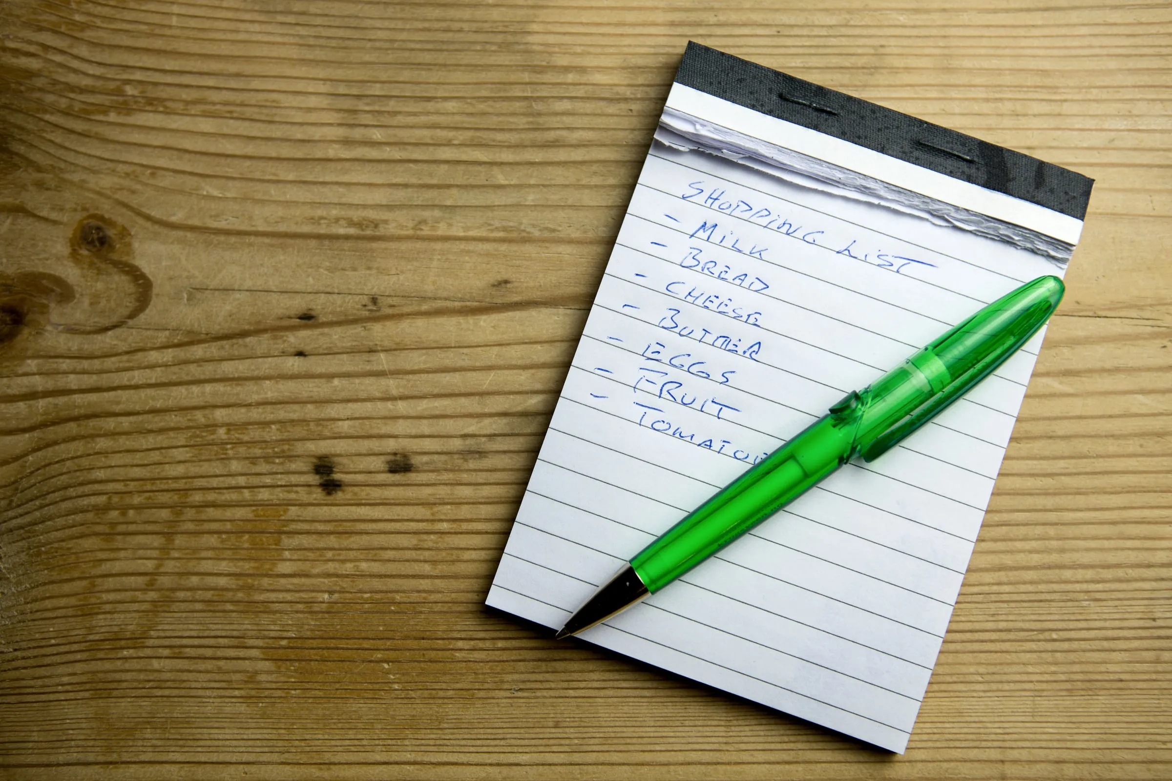 A handwritten shopping list on a notepad on a wooden table, starting with milk