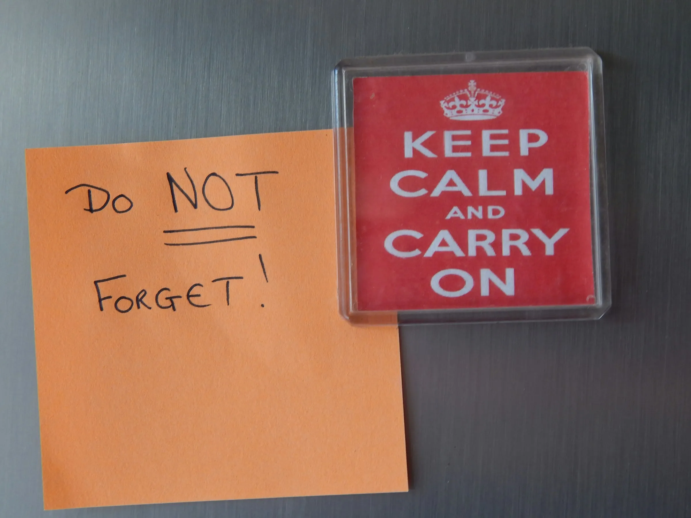 An orange sticky note reading “DO NOT FORGET!” on a fridge door, next to a fridge magnet