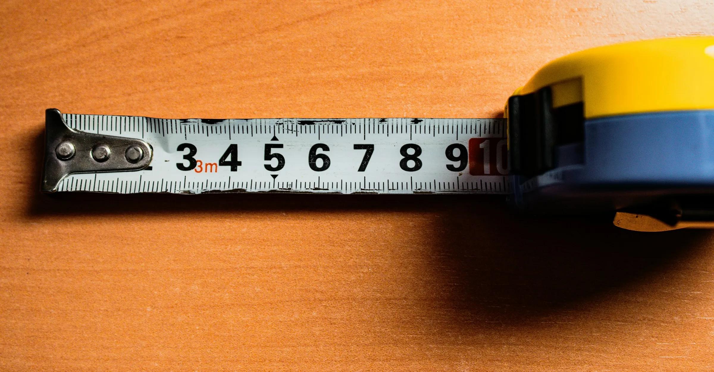 A tape measure unrolled on an orange-toned wooden table, showing its centimetre markings