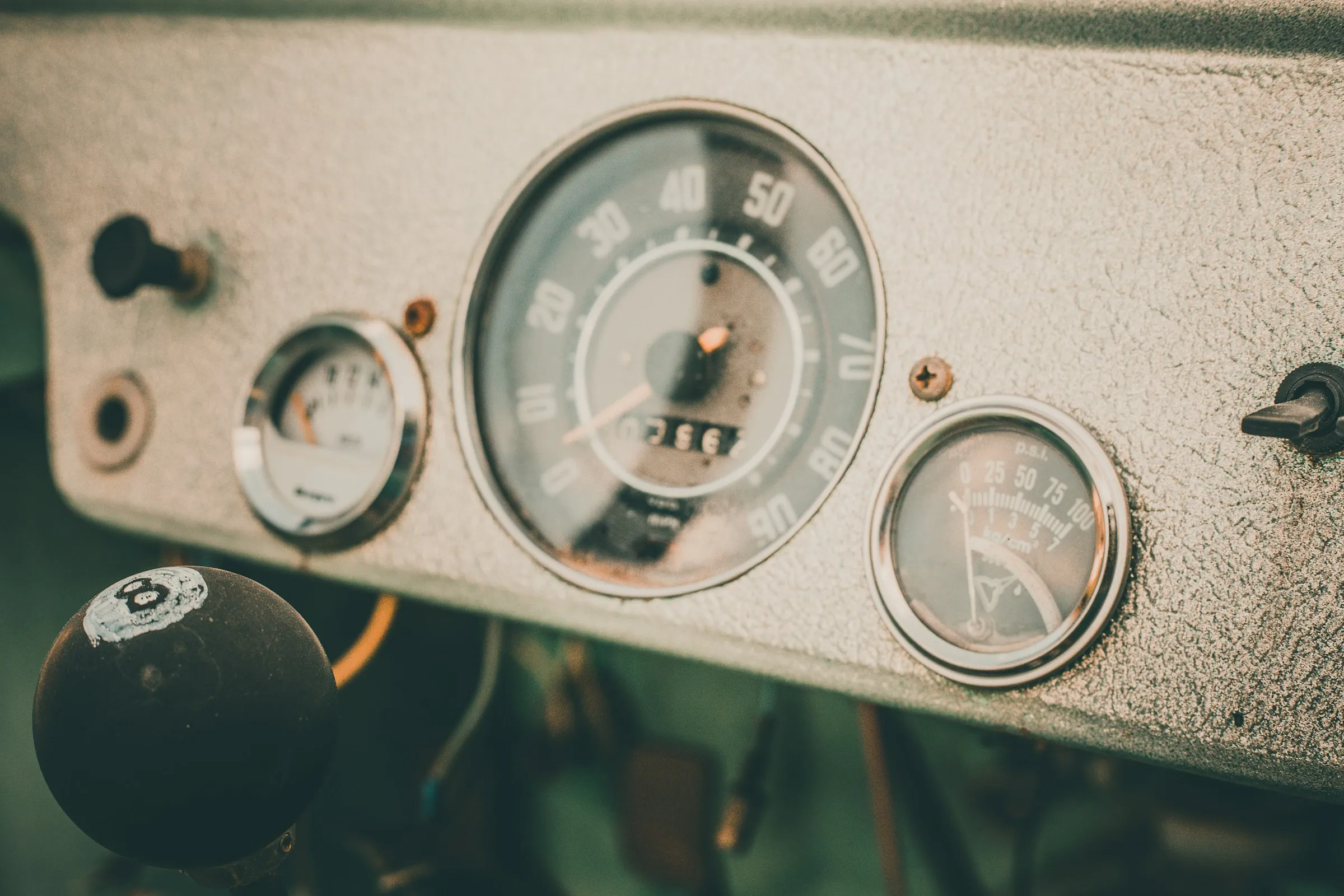 A close-up of a vintage car dashboard: an analogue speedometer with a mechanical odometer window beside a smaller gauge