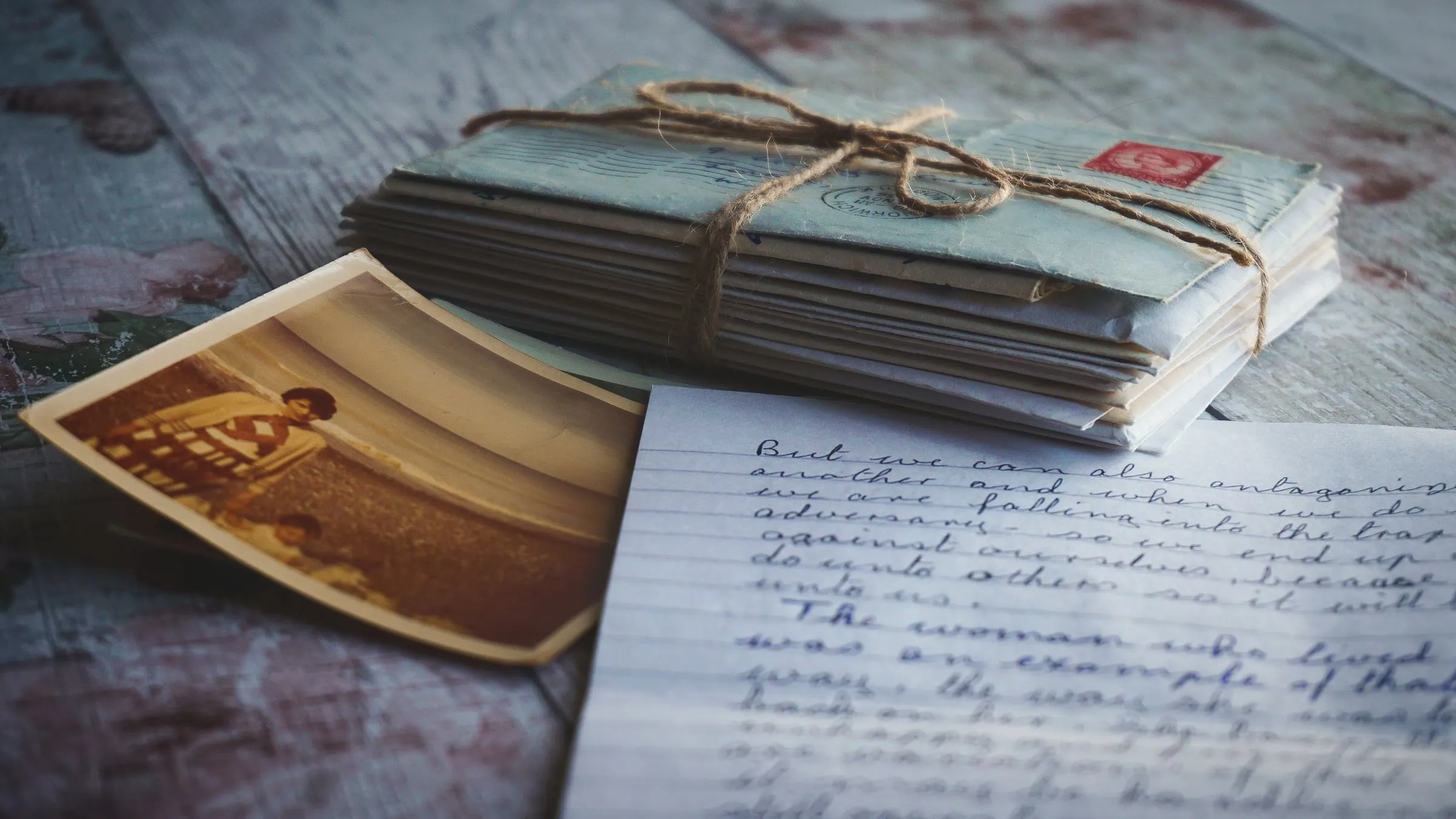 A bundle of old letters tied with twine, a faded photograph and a handwritten letter on a weathered wooden table